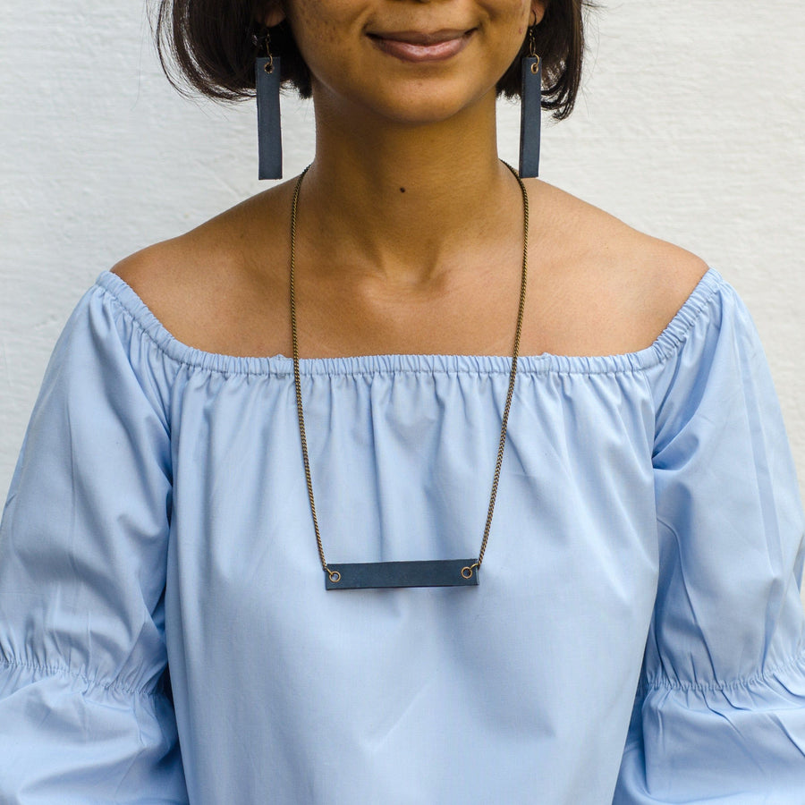 girl wearing navy blue minimalist rectangular leather earrings and neck piece with antique chain